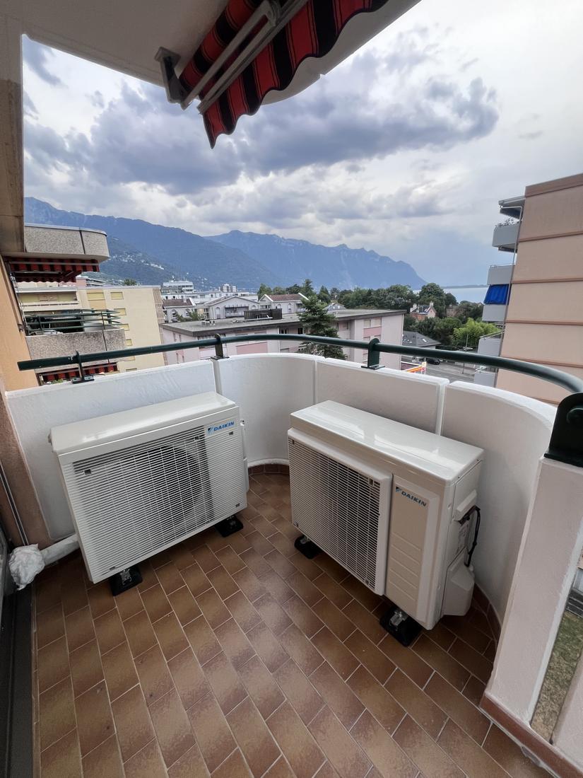 Deux groupes extérieurs Daikin alignés au fond d'un balcon d'appartement, vue sur le lac et les montagnes