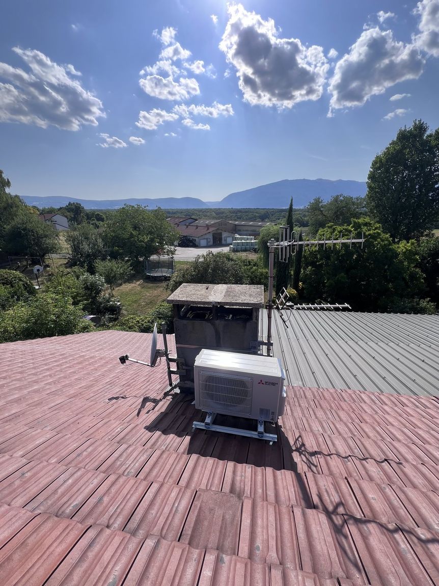 Groupe extérieur de climatisation posé sur une toiture en tuiles, montagnes en arrière-plan
